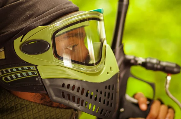 Closeup headshot man wearing green and black protection facial mask standing in profile angle, forest background, paintball concept