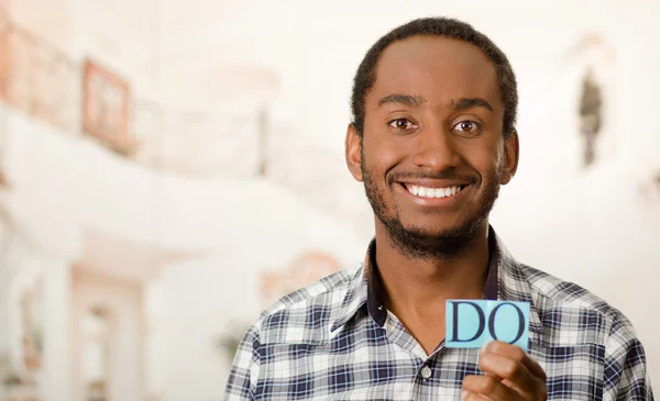 Headshot handsome man holding up small letters spelling the word do and smiling to camera