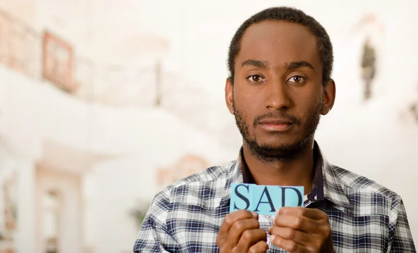 Headshot handsome man holding up small letters spelling the word sad and looking to camera