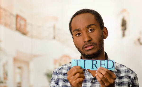 Headshot handsome man holding up small letters spelling the word tired and looking to camera