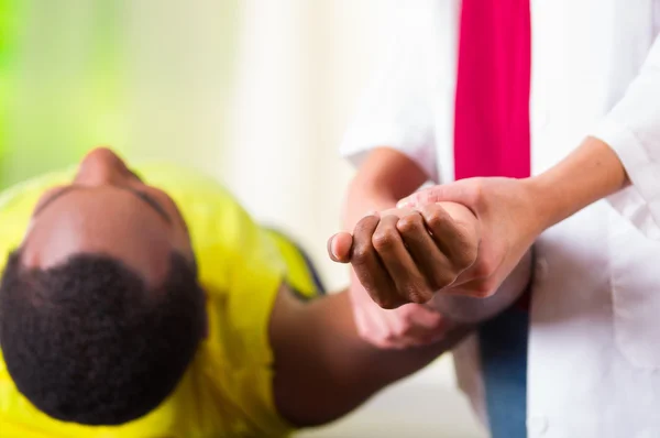 Man lying down getting physical shoulder treatment from physio therapist, patient looking into camera while her hands working on his upper arm area, medical concept