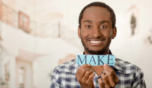 Headshot handsome man holding up small letters spelling the word make and smiling to camera