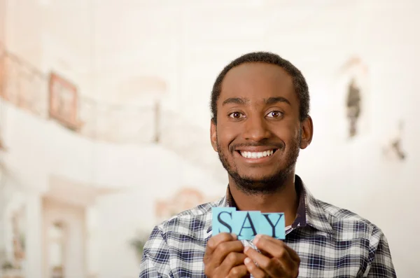 Headshot handsome man holding up small letters spelling the word say and smiling to camera