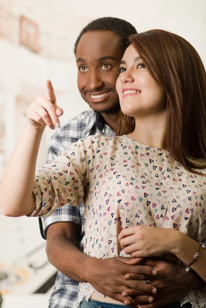 Happy interracial couple embracing and posing happily,man holding around woman from behind, white studio background