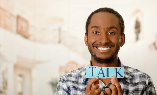 Headshot handsome man holding up small letters spelling the word talk and smiling to camera