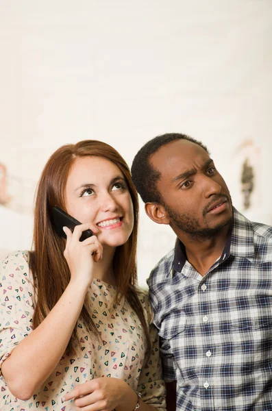 Interracial charming couple wearing casual clothes posing interacting friendly, woman talking on cell phone and man listening in, white studio background