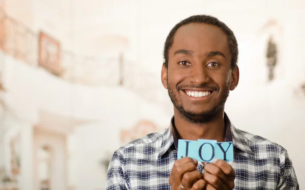 Headshot handsome man holding up small letters spelling the word joy and smiling to camera