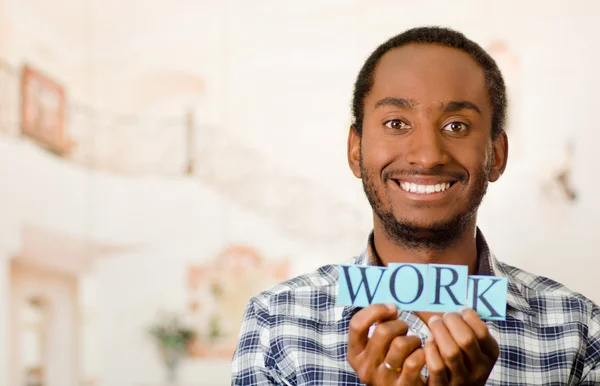 Headshot handsome man holding up small letters spelling the word work and smiling to camera