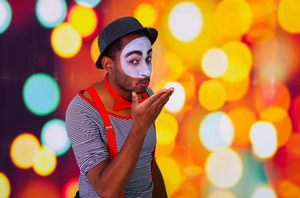 Headshot pantomime man with facial paint posing for camera using hands interacting, blurry lights background