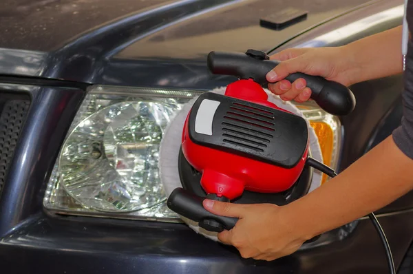 Hand with a polisher cleaning the car headlights