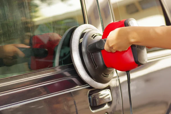 Hands holding a power buffer machine cleaning a car