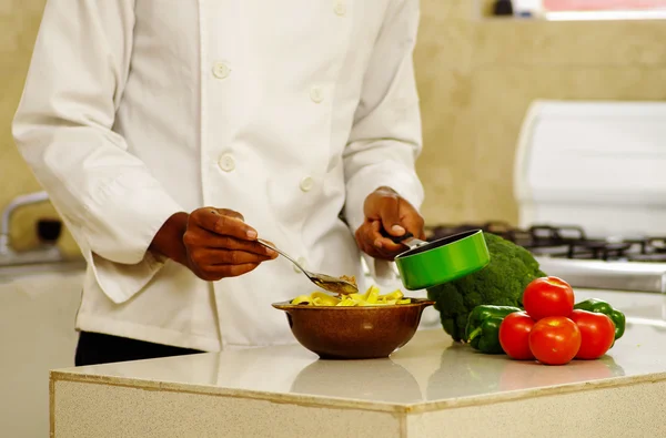 Happy chef wearing white clothes preparing bowl of food in professional kitchen, smiling while finishing last touch