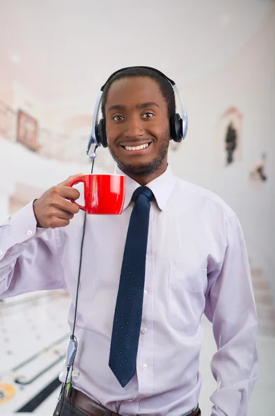 Handsome man wearing headphones with microphone, white striped shirt and tie, holding coffee mug smiling to camera, business concept