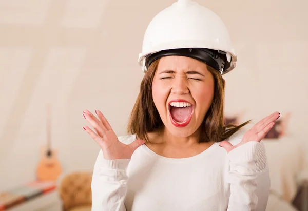 Young woman wearing construction helmet facing camera looking frustrated, upset body language