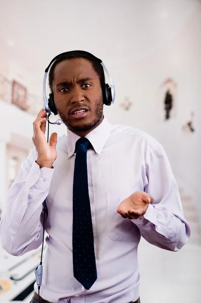 Handsome man wearing headphones with microphone, white striped shirt and tie, interacting slightly upset facial expression, business concept