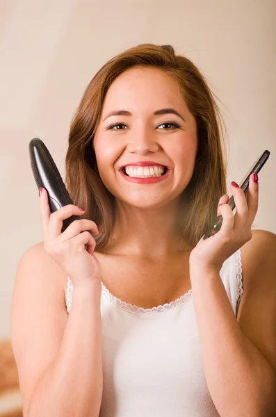 Young attractive woman wearing white top facing camera while talking on two phones smiling