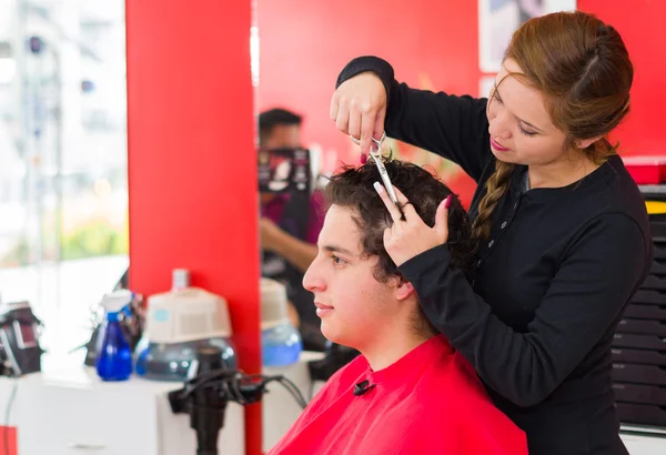 Latin man with curly hair inside a barber shop, nice hairstylist with scissors is cutting his hair