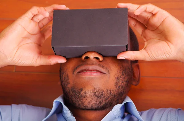 Headshot man lying down on wooden floor playing with virtual reality mobile device covering eyes