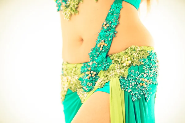 Closeup hips of bellydancer wearing blue and green colored skirt, posing performing dance moves, bright studio background