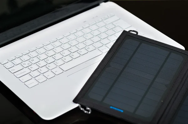 Nice black portable solar charger lying on top of white laptop, modern business technology concept, studio background