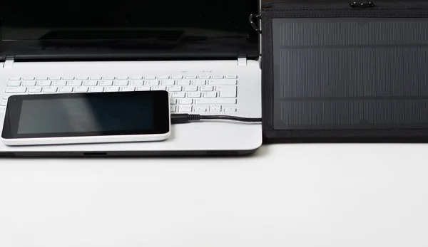 Nice black portable solar charger and a small tablet sitting on top of exclusive white laptop, modern business technology concept, studio background