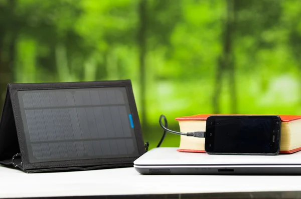 Portable solar charger sitting on white desk surface connected to tablet, modern technology concept, window garden background