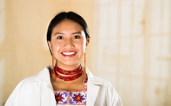 Young beautiful woman dressed in doctors coat and red necklace looking into camera smiling, egg white clinic background