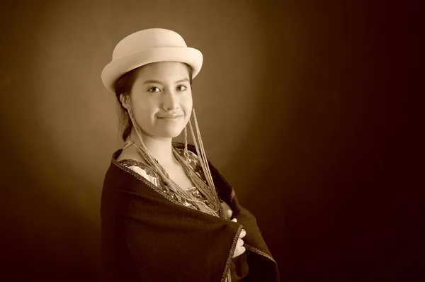 Beautiful hispanic model wearing andean traditional clothing, holding onto dark poncho on top with matching hat, smiling posing for camera, studio background, black and white edition