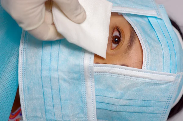 Closeup eye of woman peeking out from total facial cover, preparing for cosmetic surgery concept, doctor wiping with white pad