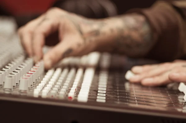 Closeup of hands covered with tattoos working on mixer console, twisting knobs, studio equipment concept