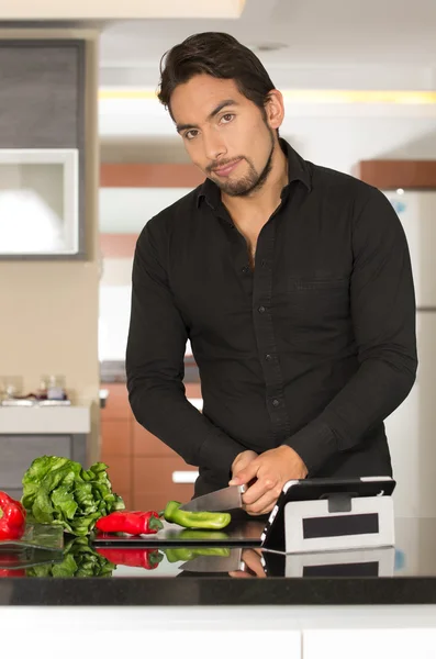 Handsome young modern man cooking healthy recipe and using tablet