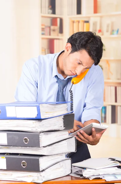Young stressed overwhelmed man with piles of folders on his desk