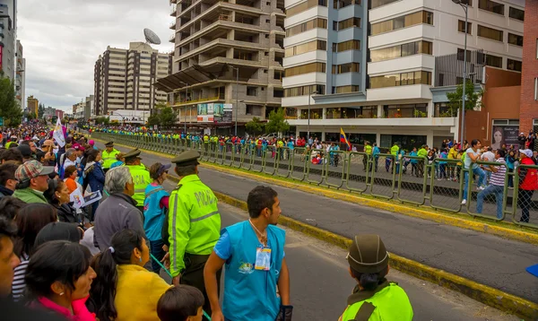 Crowds of people in Quito city street waiting for Pope Francis motorcade to arrive as numerous police officers maintains clear passage and security