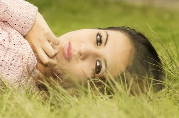 Headshot hispanic female brunette model with head resting on grass and looking sideways towards camera