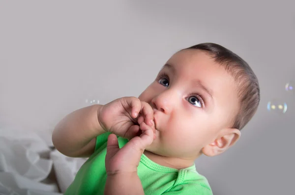 Cute baby boy in green clothing playing and having fun with bubbles hand to mouth pose