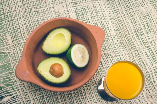 Fresh ripe avocados and lime in bowl next to glass of orange juice