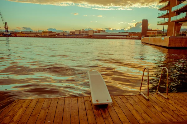 OSLO, NORWAY - 8 JULY, 2015: Diving board mounted on wooden surface above water at Aker Brygge pier area during sunset hour