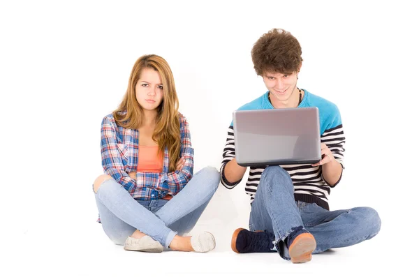 Portrait of attractive young couple in love man and woman isolated over white background sitting on floor, he looks to computer while she is mad