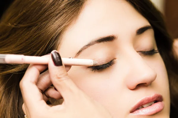 Closeup headshot brunette getting makeup treatment by professional stylist applying eyeliner
