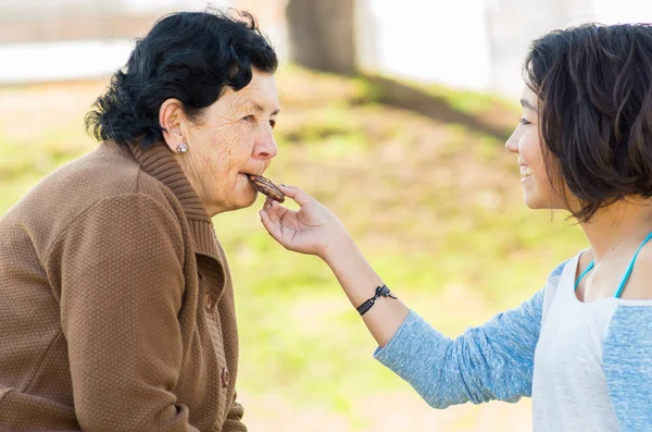 Lovely hispanic grandmother and granddaughter enjoying quality time outdoors sharing snacks