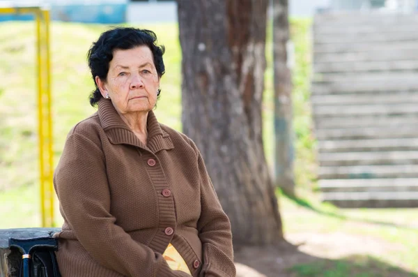 Hispanic grandmother sitting by bench wearing brown jacket waiting