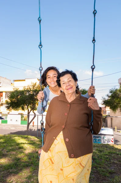 Young girl sitting on swing with grandmother in front, happily posing for camera