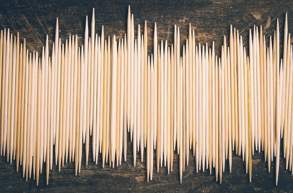 Big pile of toothpicks lying in an uneven horisontal line on dark wooden surface