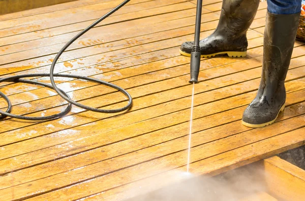 Man wearing rubber boots using high water pressure cleaner on wooden terrace surface