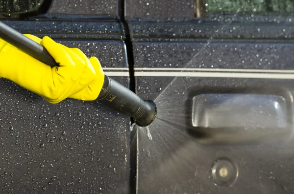 Arm with yellow glove holding high pressure water cleaner and using it on car door windows