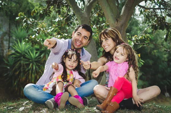 Beautiful hispanic family of four sitting outside on grass engaging in conversations while posing naturally and happily