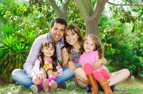 Beautiful hispanic family of four sitting outside on grass engaging in conversations while posing naturally and happily