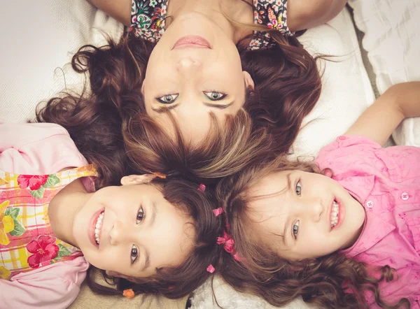Young adorable hispanic sisters and mother lying down with heads touching, bodies spread out different directions closeup
