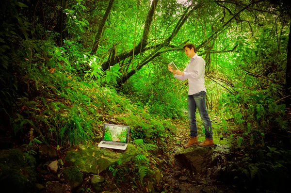 Young handsome man using tablet and laptop with great internet connectivity in the jungle