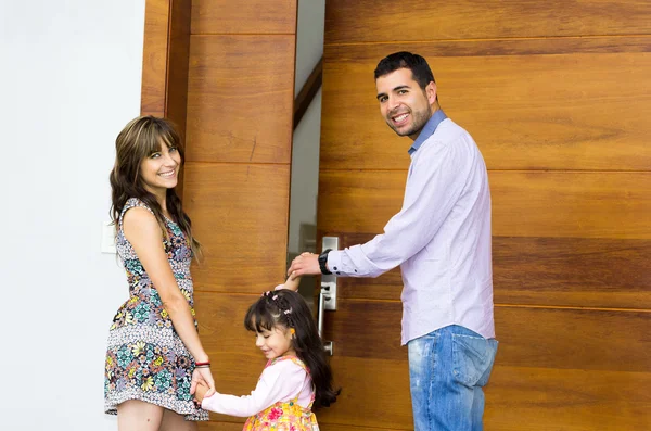 Adorable hispanic family of three posing for camera outside front entrance door while entering house